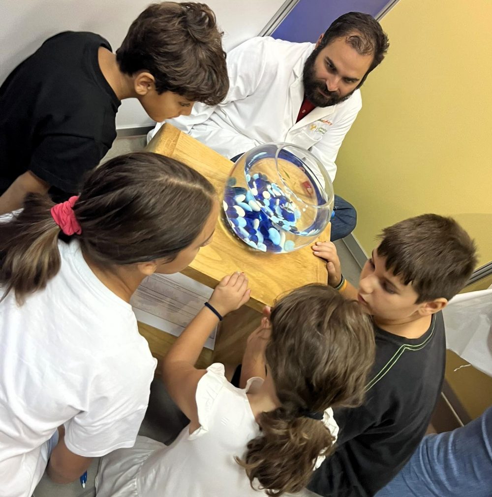 A scientist shows a group of children a fishbowl with zebrafish.