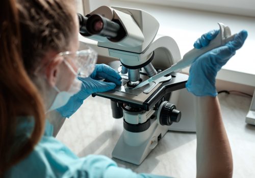 woman laborant working with microscope holding automatic pipette