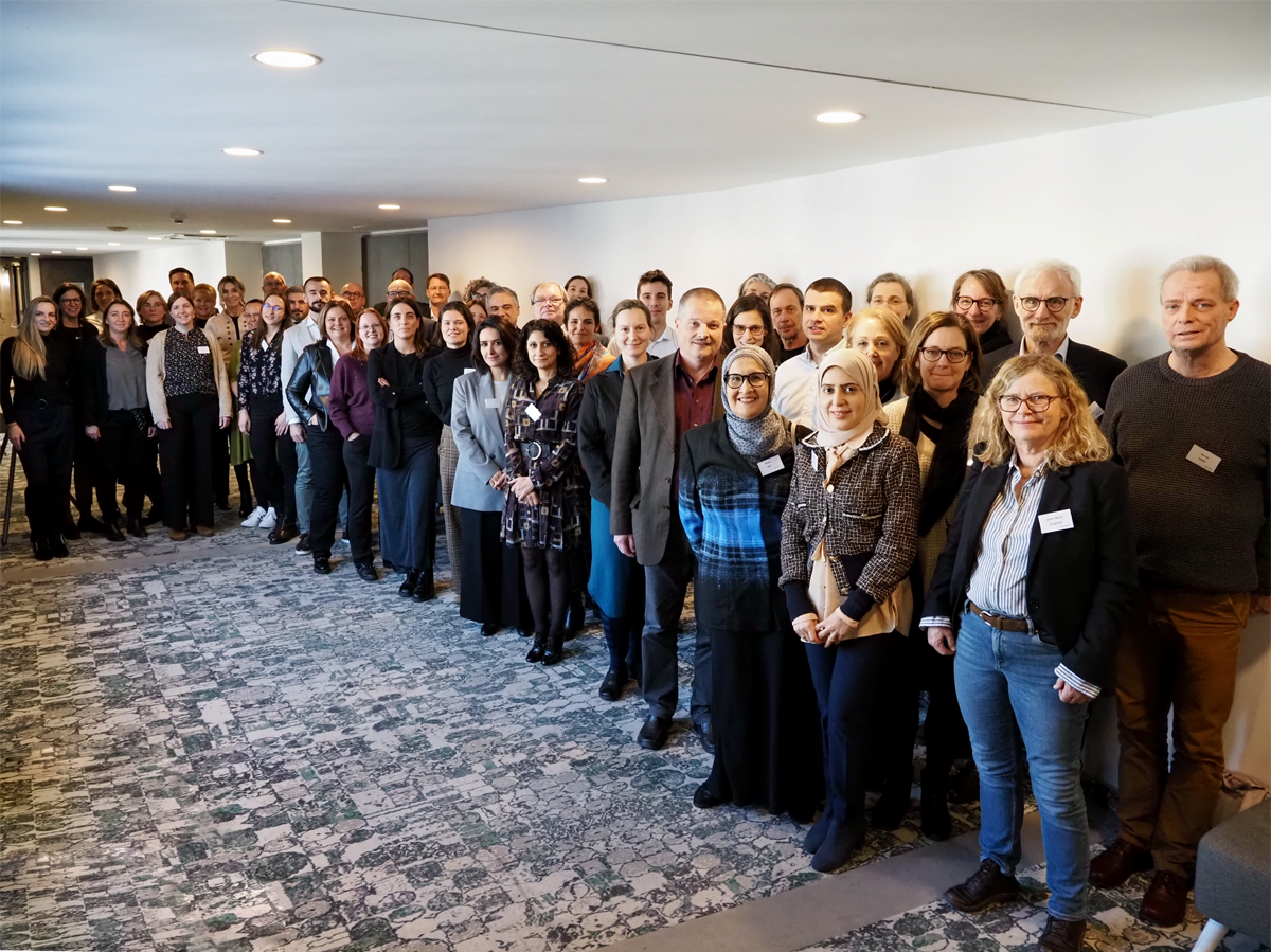 A large group of people are gathered in a curve shape down a hallway. They are looking at the camera and smiling.