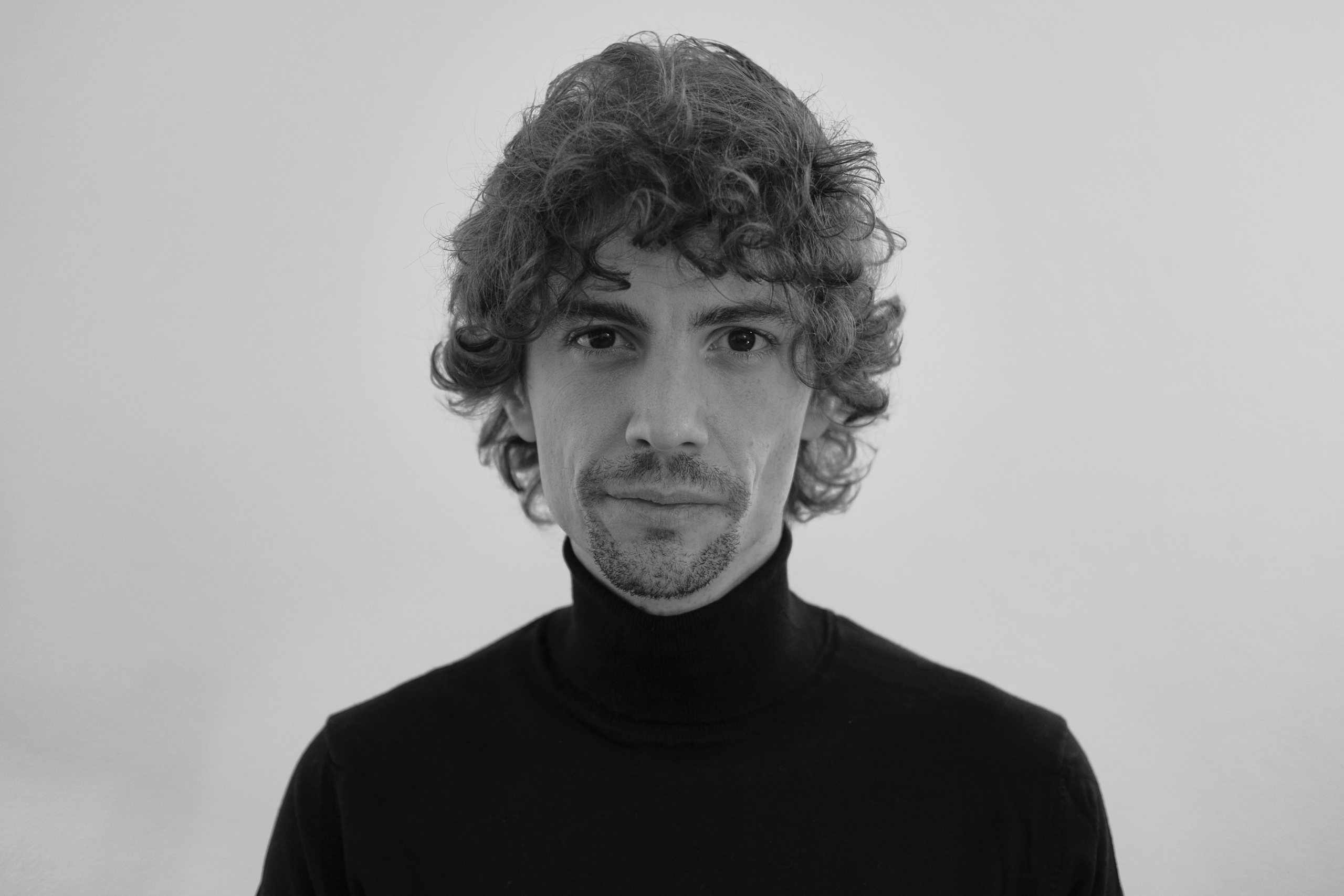 the black and white picture of a man with curly hair looking at the camera