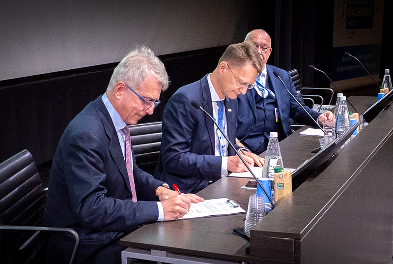 Two men sitting at a podium signing a Memorandum of Understanding.